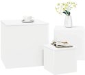 Drie witte kubusvormige bijzettafels, één met een kopje koffie, één met tijdschriften, en één met een vaas bloemen.