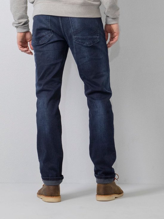 Achterkant van een man in donkerblauwe, regular tapered fit jeans met lichte wassing. Broekspijpen omgeslagen.
