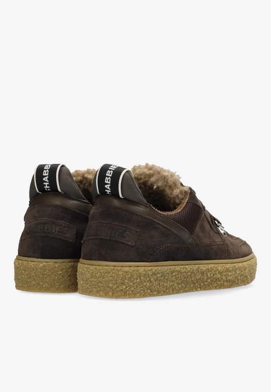 Achterkant van donkerbruine suède sneakers met crèmekleurige zool en teddy voering. Zwarte bandjes met "SHABBBIES" logo op de hiel.