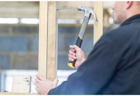 Man met Stanley klauwhamer met geel-zwarte handgreep slaat een spijker in hout.
