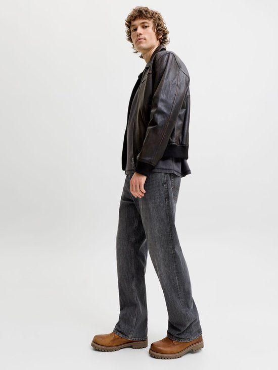 Zijaanzicht van een model in een grijze jeans en bruine schoenen.