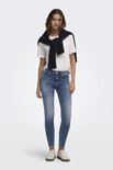 Vrouw in blauwe skinny jeans met lichte wassing, rafelige zoom en witte top.