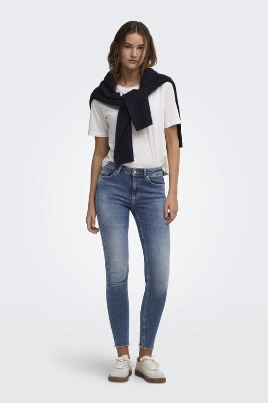 Vrouw in blauwe skinny jeans met lichte wassing, rafelige zoom en witte top.