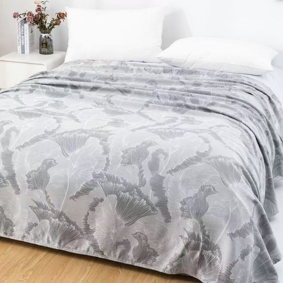 Een bed met grijs en wit gebloemd textiel, met twee witte kussens en een nachtkastje met een vaas bloemen.