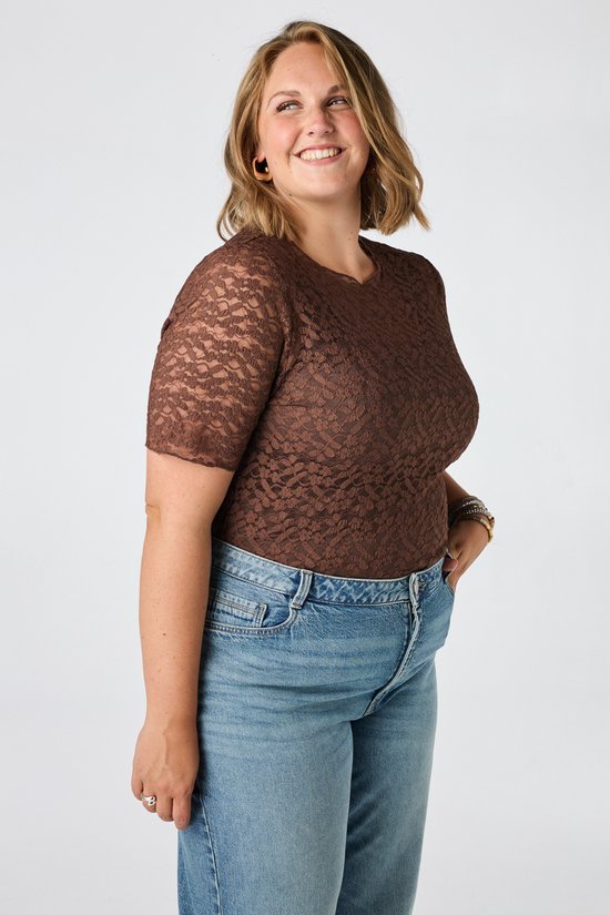 Model lacht, staand in bruine kanten top en jeans.