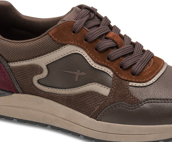 Close-up van de zijkant van de bruine Tamaris sneaker, met lederen panelen, mesh en een klein kruislogo.