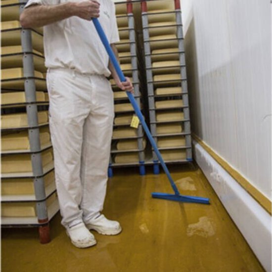 Man in witte kleding gebruikt een blauwe vloertrekker met steel om een gele vloer schoon te maken.