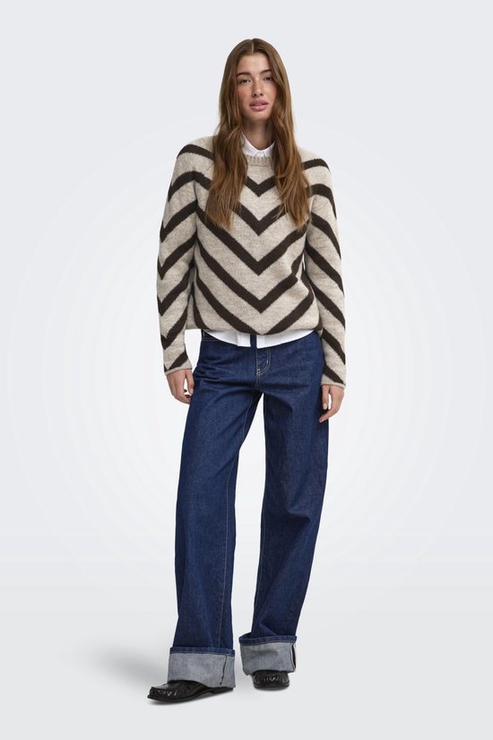 Lichtbruine trui met donkerbruine chevronprint, gedragen door een model met een witte blouse en jeans.