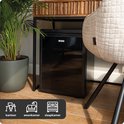 Zwarte BREND koelkast naast een plant en een stoel, met icoontjes voor kantoor, woonkamer en slaapkamer.