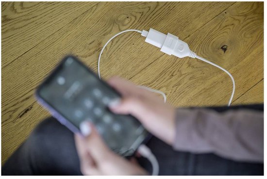 Een persoon laadt een smartphone op met een wit verlengsnoer op een houten vloer.