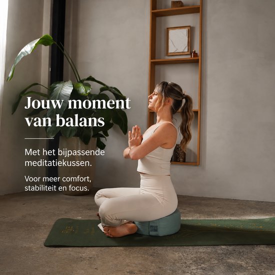 Vrouw in beige outfit mediteert op een donkergroene yogamat met gouden plantenprint en een lichtgroen meditatiekussen.
