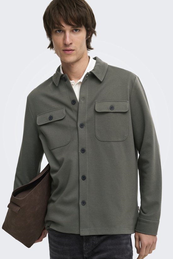 Man met olijfgroene utility blouse met twee borstzakken, wit poloshirt en donkerbruine tas.