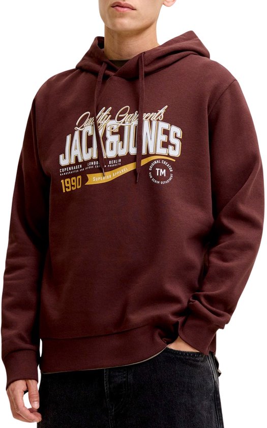 Een man draagt een bruine hoodie met capuchon en een 'Jack & Jones' logo op de borst, met een donkere spijkerbroek.