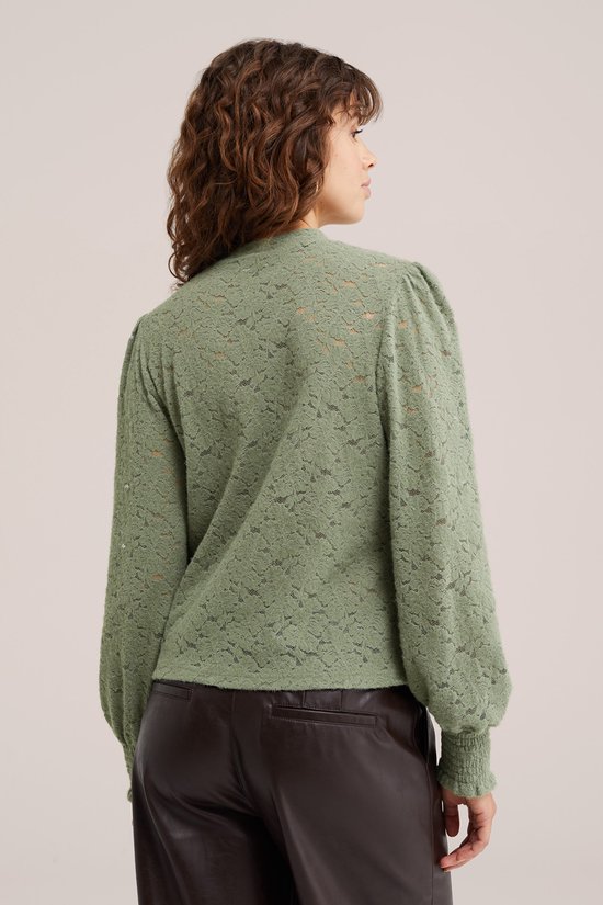Lichtgroene kanten top met pofmouwen, hoge hals en smalle manchetten, gedragen door een model met donkerbruine broek.