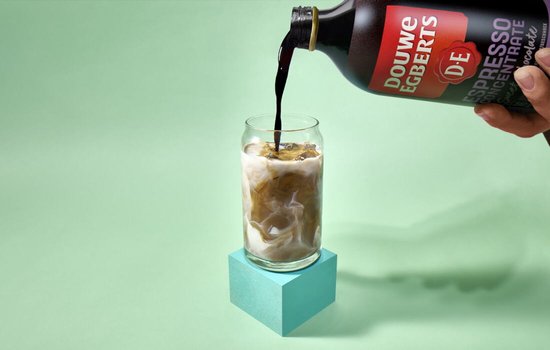 Douwe Egberts espresso concentrate, zoete chocolade smaak, wordt in een glas met ijs en melk gegoten.