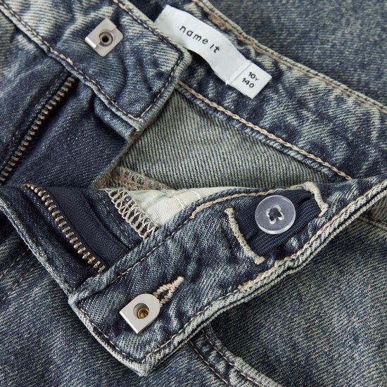 Sluiting van een lichtblauwe wijde jeans: knopen, ritssluiting, en verstelbare tailleband met knoopje.