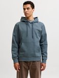 Man met blauwgrijze hoodie met kangoeroezak en 'JACK & JONES' logo. Draagt een bruine broek.