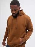 Close-up van een man met bruine hoodie, hand in de zak.