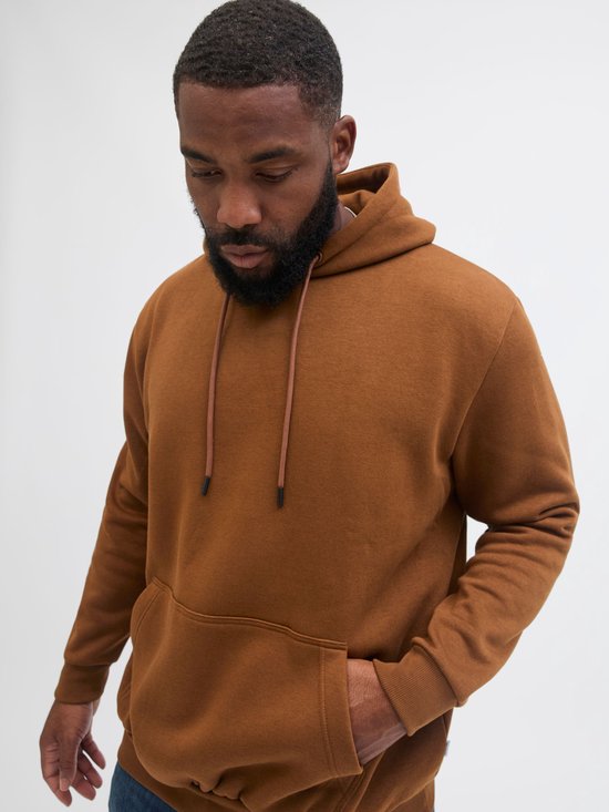 Close-up van een man met bruine hoodie, hand in de zak.