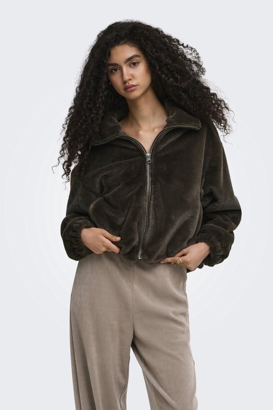Model met krullend haar draagt een donkerbruine teddy jas met ritssluiting.