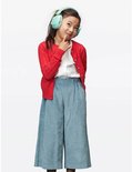 Een jong meisje met een rode vest, wit shirt en blauwe corduroy culottes draagt een mintgroene koptelefoon.