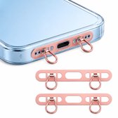 Detailopname van een telefoonhoesje met rosé gouden metalen adapters aan de onderkant. Twee lanyard houders met dubbele ringen liggen ernaast.