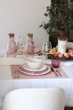 Table dressée avec sets de table roses, vaisselle blanche, bouteilles roses et un verre rose.