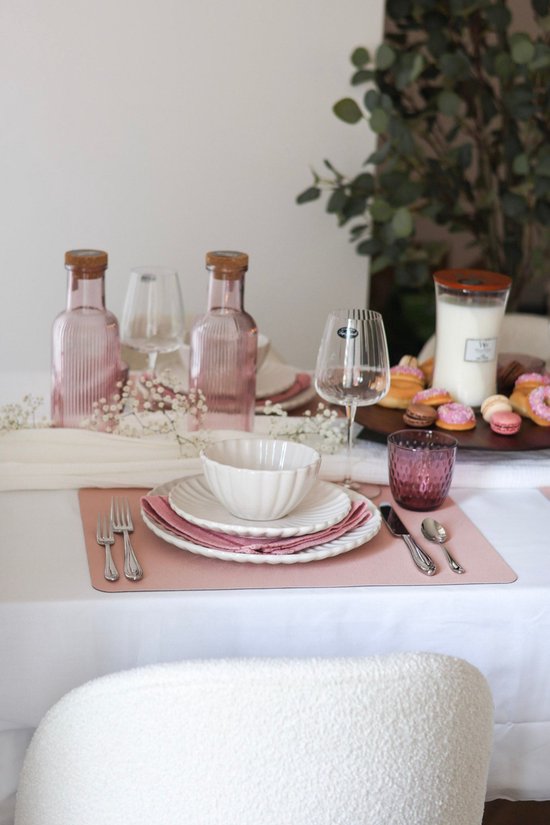 Table dressée avec sets de table roses, vaisselle blanche, bouteilles roses et un verre rose.