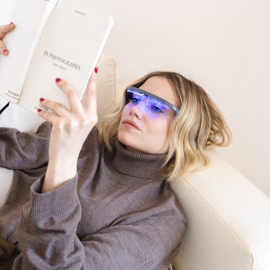 Vrouw met blond haar, lezend, draagt een AYOlite lichttherapiebril die blauw licht uitstraalt.