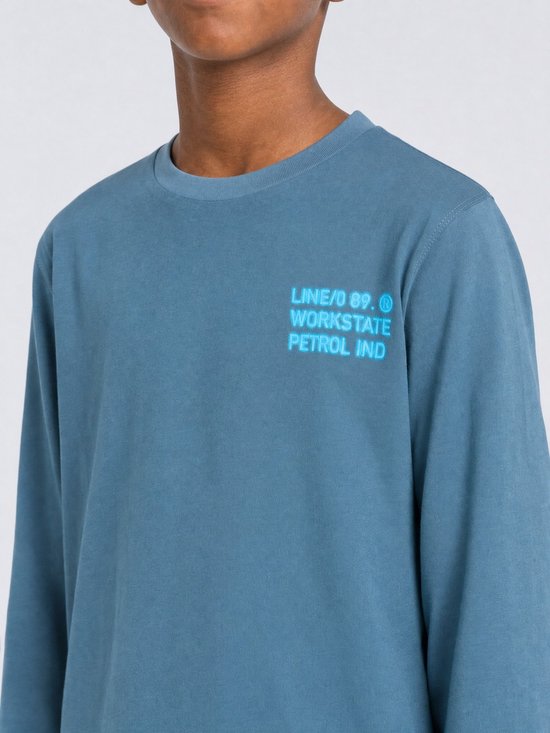 Detail van een blauw longsleeve T-shirt met 'LINE/0 89. WORKSTATE PETROL IND' opdruk op de borst.