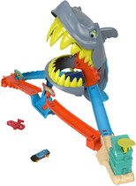 Hot Wheels speelset met haai die de baan opslokt, met oranje en blauwe racebanen, en twee speelgoedauto's.
