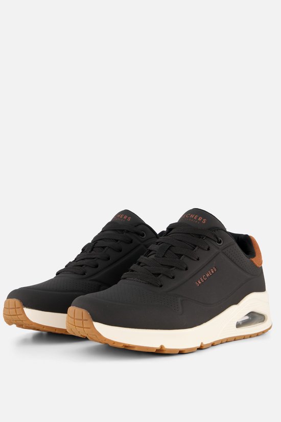 Zwarte Skechers sneakers met bruine accenten en crèmekleurige zolen, vanuit een hoek bekeken.