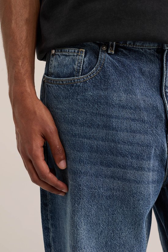 Close-up van een loszittende, blauwe spijkerbroek met een muntzakje en voorzak. De stof heeft een denim textuur.