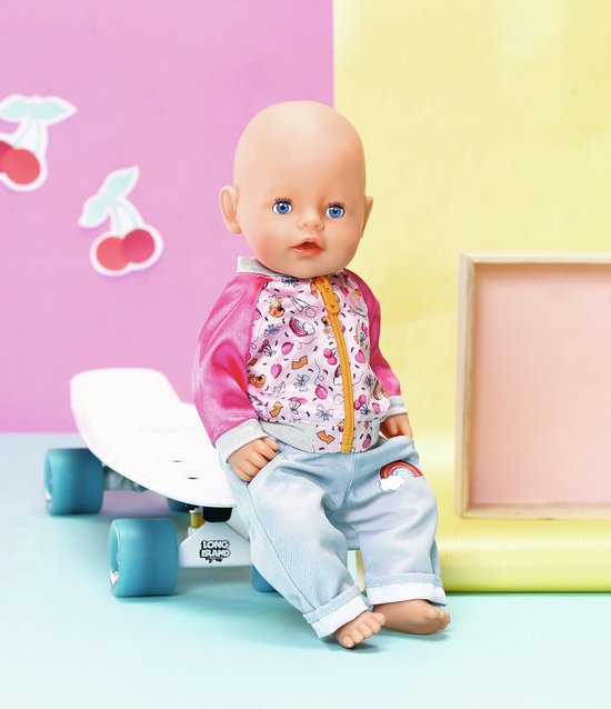 BABY born pop zittend op een skateboard. Draagt roze jasje met print en lichtblauwe broek met regenboog.