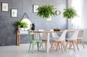 Eetkamer met grijze muren, planten en witte stoelen aan een houten tafel.