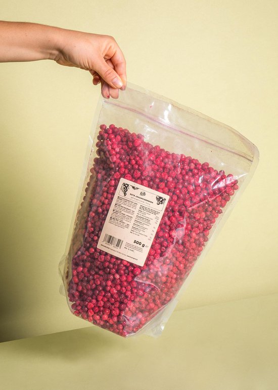 Hand die een plastic zak met gevriesdroogde rode bessen vasthoudt tegen een gele achtergrond.