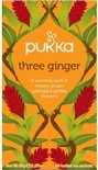 Pukka three ginger biologische thee verpakking met rode gemberbloemen en groene bladeren, op een oranje achtergrond.