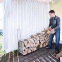 Man laadt hout in een zilverkleurige houtopslag naast een witte schutting.