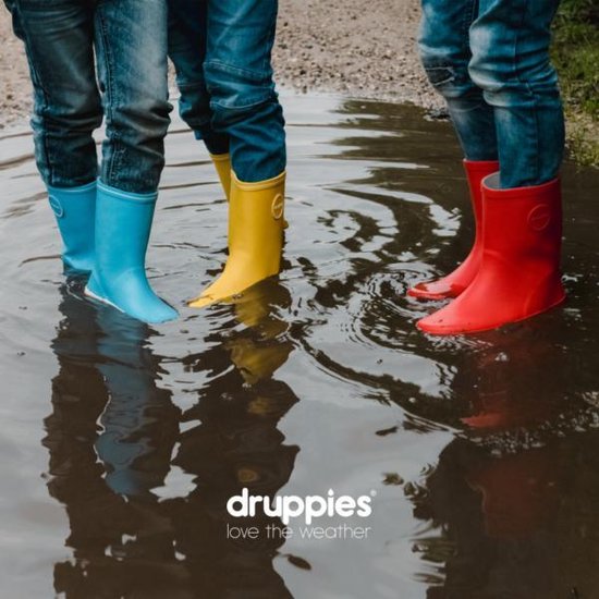 Blauwe, gele en rode rubberen laarzen voor kinderen in een waterplas. Denim broeken zichtbaar.