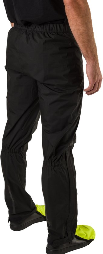 Zicht op de achterkant van een man die een zwarte AGU regenbroek draagt met gele overschoenen.
