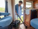 Man met blauw overhemd stofzuigt camper met grote groene en zwarte stofzuiger.