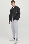 Man met lichtgrijze joggingbroek en witte sneakers, gedragen met een donkere jas.