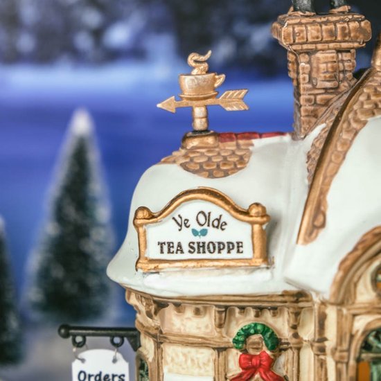 Close-up van een besneeuwd Lemax 'Ye Olde Tea Shoppe' gebouw met gouden windvaan.