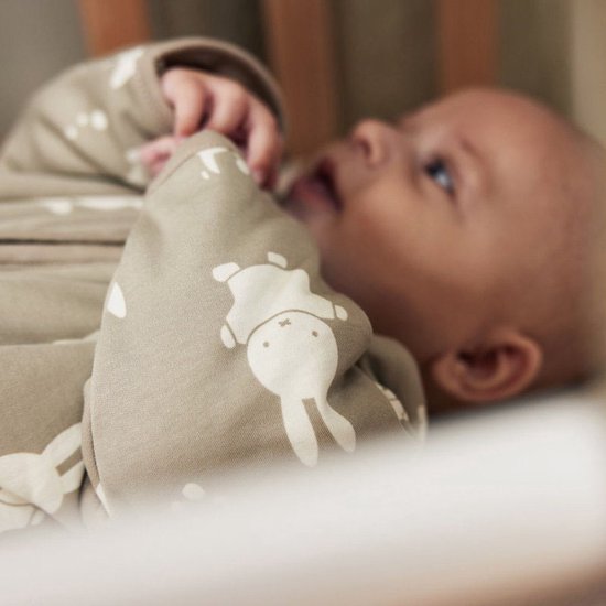 Close-up van een baby in een olijfgroene slaapzak met Miffy print.