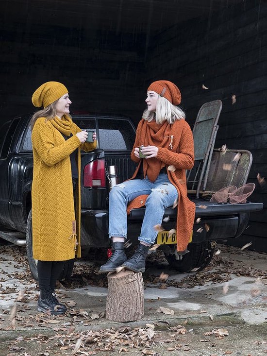 Twee vrouwen bij een pick-up truck. De ene vrouw draagt een lange mosterdgele gebreide jurk, de ander een oranje outfit.