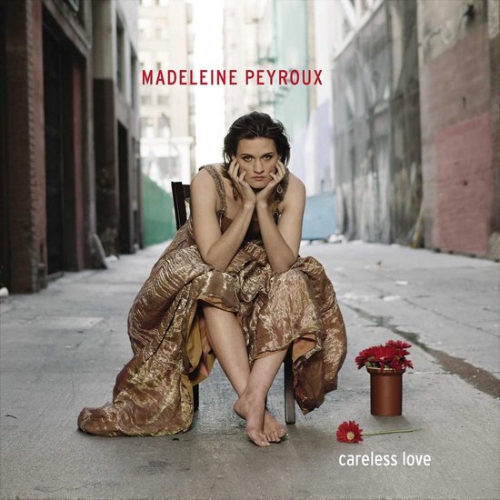 Madeleine Peyroux in een gouden, glinsterende jurk, zittend op een stoel in een steegje. 'careless love' tekst op de voorgrond.
