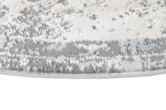 Gros plan du bord rond d'un tapis gris à texture usée avec de subtils accents bleus.