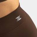 Close-up van bruine sportbroek met zilveren logo en stiksels aan de zijkant.