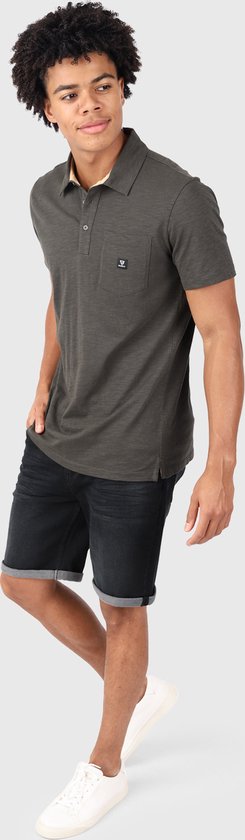 Jonge man in een donkergrijs poloshirt met opgestoken kraag, zwarte jeansshort en witte sneakers.