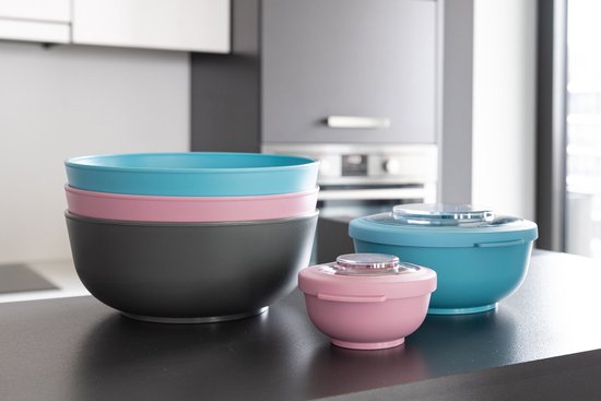 Trois grands bols, empilés et côte à côte, en rose, bleu et gris, sur un comptoir sombre.